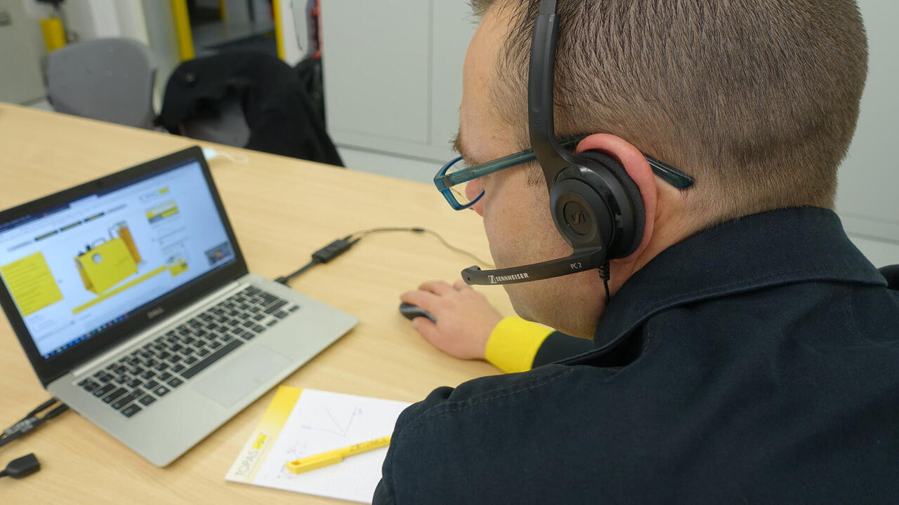 Mitarbeiter mit Headset, Laptop und Schreibgeräten am Tisch