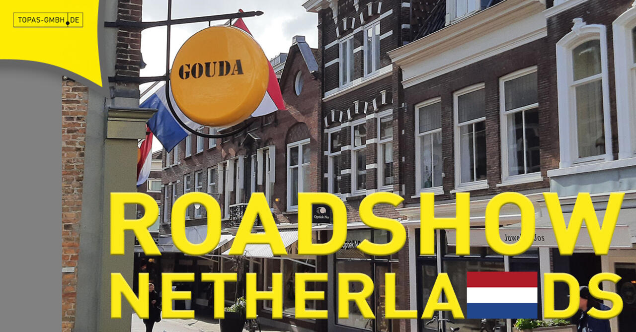 Straßenansicht in Gouda mit Käseschild im Vordergrund, Überschrift Roadshow Netherlands mit Flagge