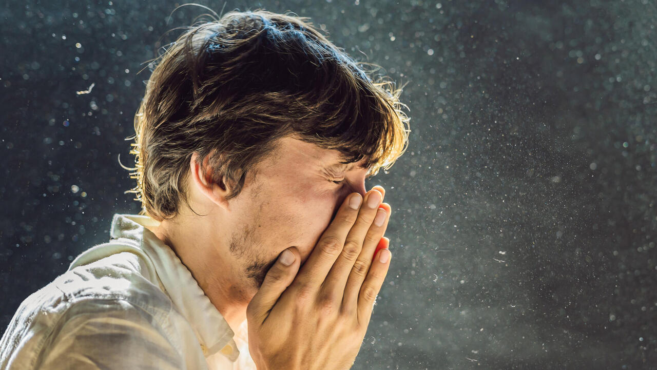 Sneezing human in particle cloud against dark background