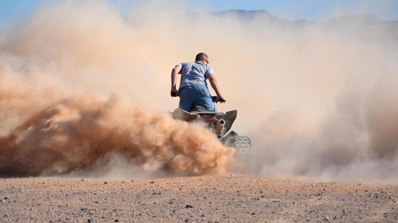 Rider on a quad bike in dust cloud in the desert