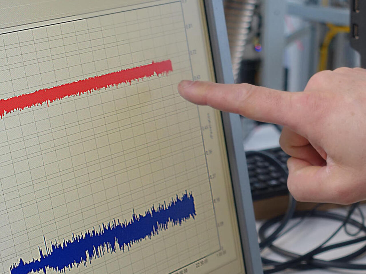 Tastatur und Monitor mit Graphen, auf den eine Person mit dem Finger zeigt