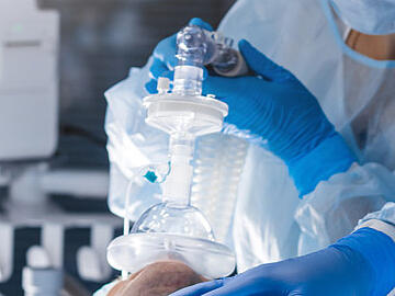 Operating room with doctors bending over a patient, medical filter in the middle over the nose for ventilationn beugen, mittig Medizinfilter über der Nase zm Beatmen
