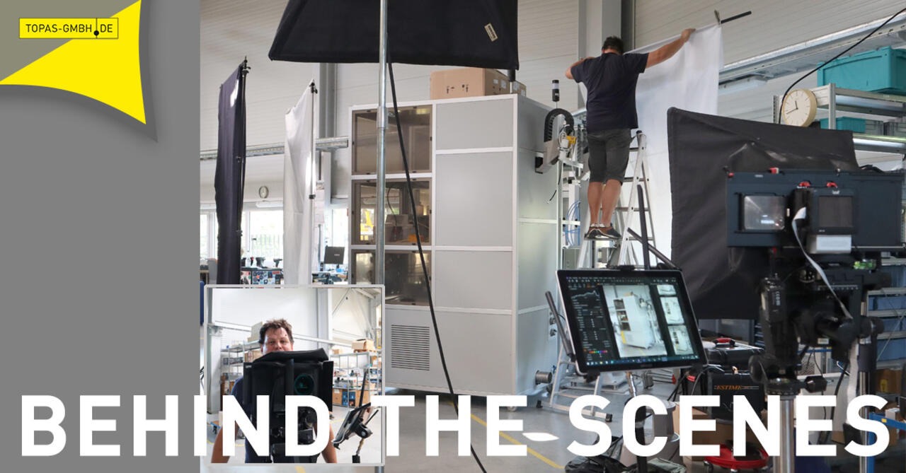 Fotoshooting in Produktionshalle: Fotograph mit Leinwand auf Leiter neben Prüfsystem