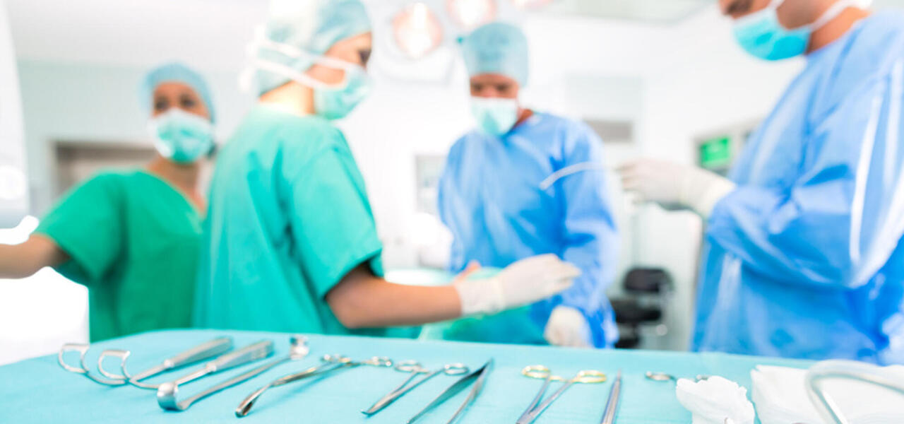 Doctors and nurses at the operating table, which is in the foreground with many instruments on it 