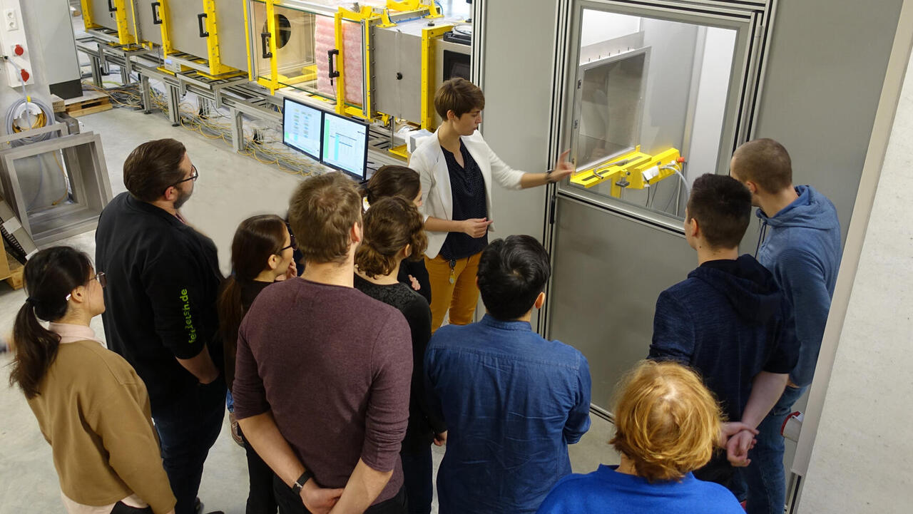 Group of people next to a viewing window of a test bench chamber with a person in front of the group who has been arrested