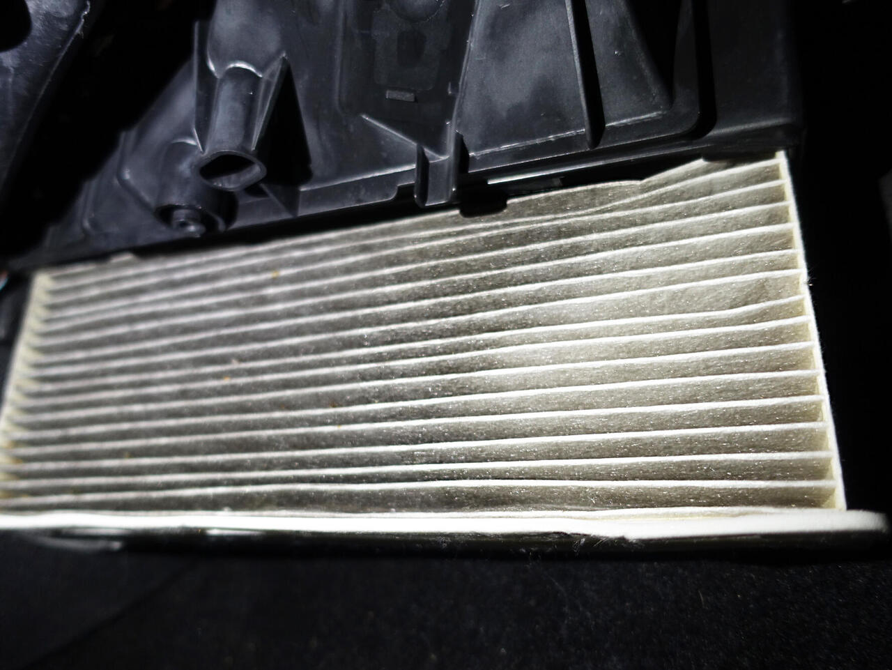 White cabin air filter pulled out of holder in the foot area of the car