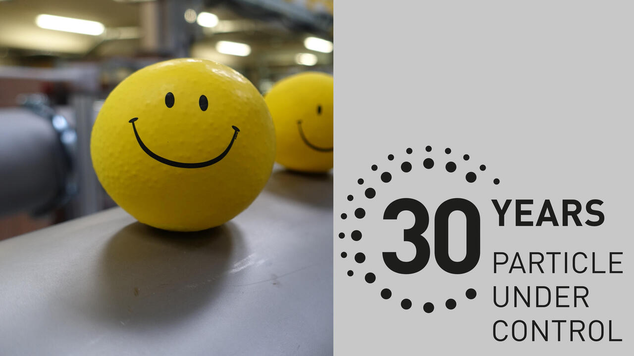 Produktionshalle mit gelben Smileybällen auf Kanal, daneben auf grauem Untergrund "30 Jahre Topas"-Label