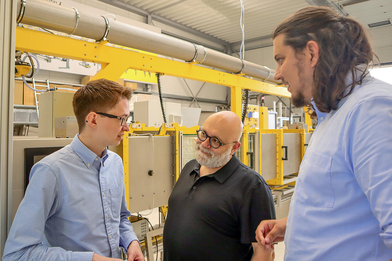 Production site with test system, three persons in a conversation in front of it