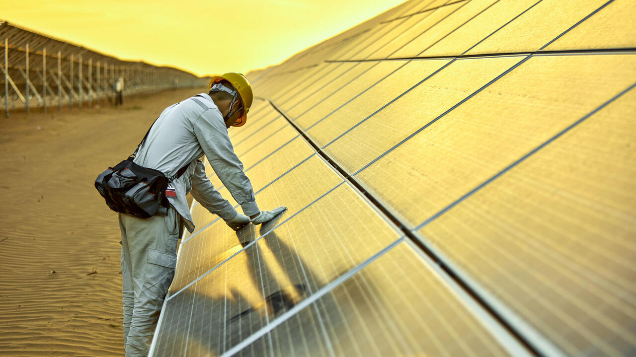 Ingenieur prüft Photovoltaikanlage in Wüste vor gelbem Himmel